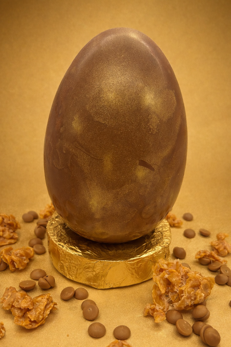 Chocolate egg with gold base surrounded by chocolate pieces on a gold background