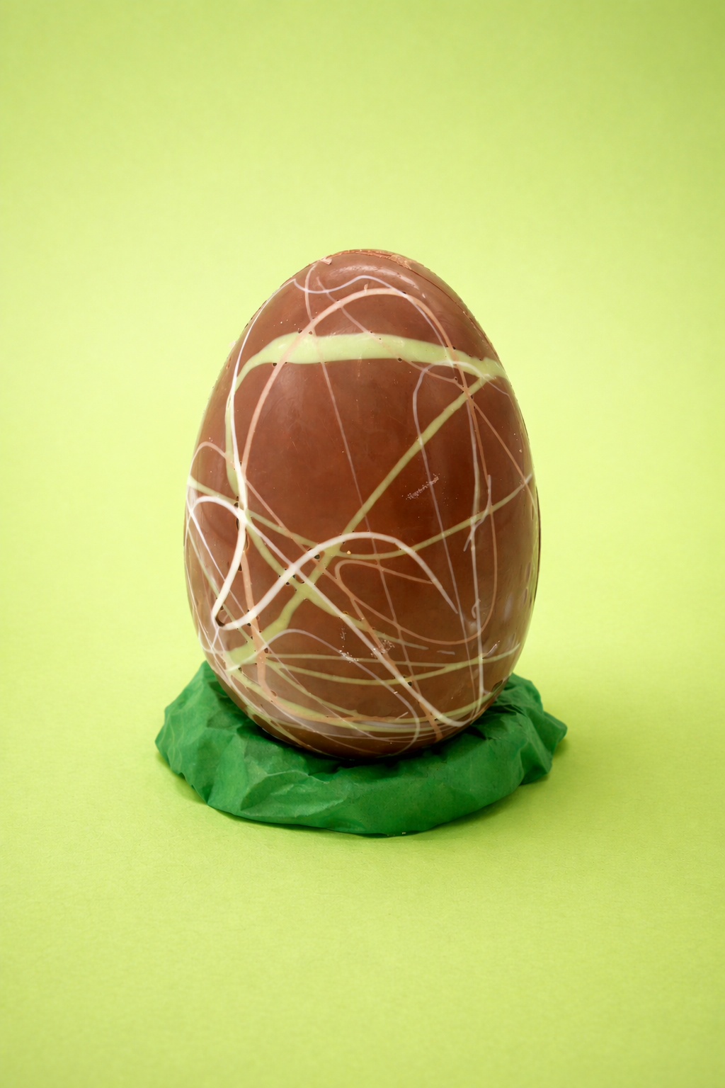 Chocolate egg with white drizzle on a green base against a light green background
