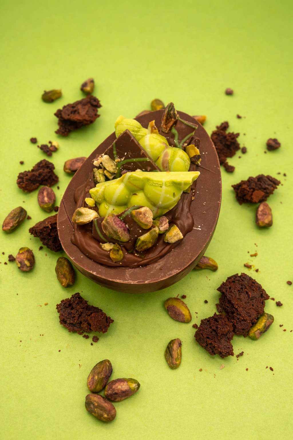Chocolate half egg with pistachios on a green background