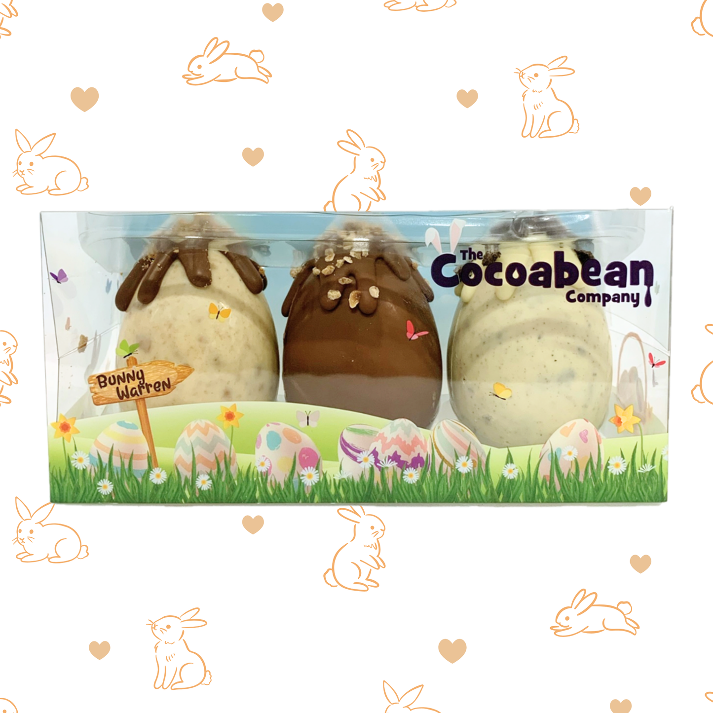 Three chocolate eggs in a clear box with 'The Cocoabean Company' branding, surrounded by Easter-themed illustrations on a white background.